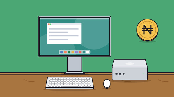 A Mac mini on a desk beside a monitor, keyboard and mouse, with a naira coin